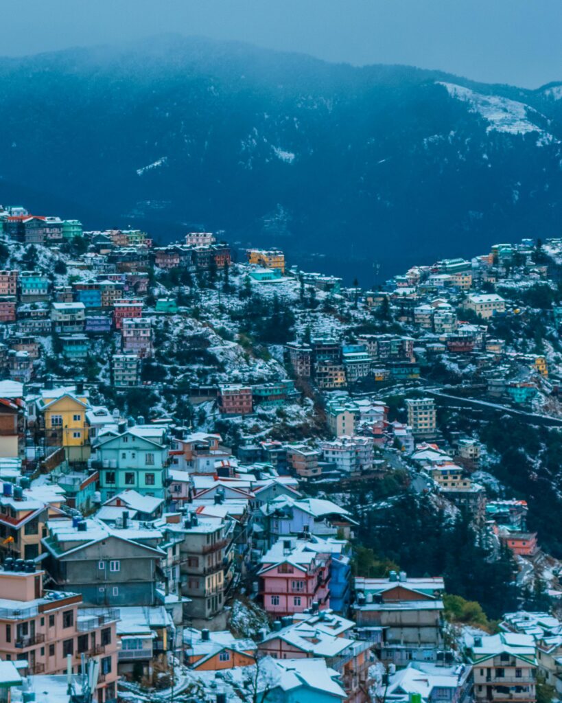 A stunning winter view of Shimla, India with colorful snow-covered buildings and mountain backdrop.